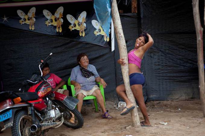 In this May 5, 2014 photo, a sex worker who is employed by an informal bar playfully sticks out her tongue while posing for a photo, outside her place of her employment in La Pampa in Peru's Madre de Dios region. Since artisanal gold mining took hold in La Pampa, miners began carving a lawless, series of ramshackle settlement out of the Amazonian jungle territory in 2008. (AP Photo/Rodrigo Abd) ORG XMIT: ABD120